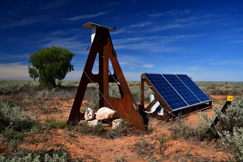Rusted-steel Desert Fireball Network observatory with solar panel on red earth under blue sky