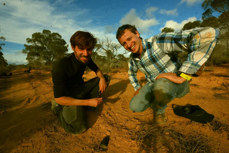 Two researchers kneeling beside a freshly recovered meteorite in the outback